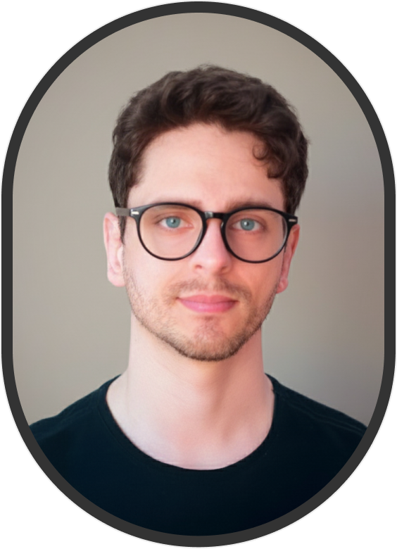 Minha foto. Homem branco, cabelo médio loiro escuro, sorrindo levemente para a câmera, usando uma camiseta preta.